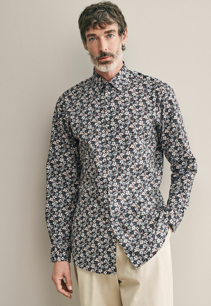 Blumenhemd mit Knopfleiste, das einen dunkelblauen Hintergrund mit kleinen weißen, rosa und grünen Blumen hat; langärmlig und mit klassischem Kragen.