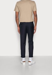 Světle béžové tričko, námořnické kalhoty, bílé tenisky s hnědým akcentem. Kalhoty mají slim fit a ohrnuté manžety, s viditelnými zadními kapsami.