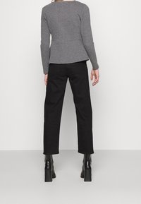 Haut à manches longues gris texturé avec une taille peplum, associé à un pantalon noir taille haute et des bottines noires à talons blocs.