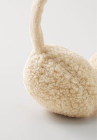 Cache-oreilles en polaire beige avec une surface douce et texturée, et un bandeau incurvé, conçu pour la chaleur et le confort.