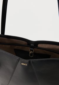Sac cabas BOSS en cuir noir avec doublure intérieure marron, logo doré à l'avant et fermoir en métal doré à l'intérieur.
