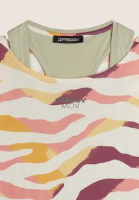 Top firmato Freddy con base crema, decorato con motivi ondulati in rosa, giallo e marrone scuro, sovrapposto a un tank top verde.