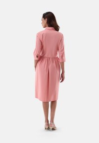 Abito rosa a lunghezza ginocchio realizzato in tessuto morbido con vita arricciata, colletto e maniche a tre quarti.