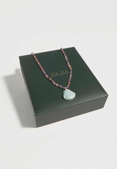 Χρωματιστό κολιέ με χάντρες και πετρόλ μπλε χαραγμένο μενταγιόν που ακουμπά σε ένα σκούρο πράσινο κουτί με χρυσή επιγραφή "JIAJIA".