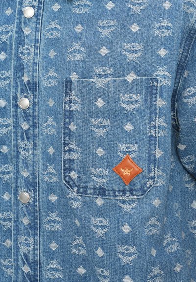 Jeansskjorta i ljusblå färg med en texturerad nedtoning av kronor och diamanter, metallknappar med tryck och en logotyp i brunt läder.