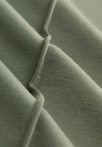 Tessuto di cotone in verde tenue che mostra una texture liscia, con dettagli di cucitura e un design piegato che enfatizza la sua forma.