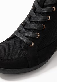 Černé tenisky s tkanou textilní špicí, semišovými bočními panely a černými tkaničkami provlečenými bronzovými kroužky.