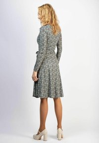 Langarmige jurk van een blauw, beige en groen gemêleerd stof. Aansluitende taille met een uitlopende rok. Gedragen met beige plateauhakken.