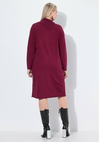 Abito midi color bordeaux con maniche lunghe e scollatura a collare. Tessuto liscio, taglio dritto, abbinato a stivali al ginocchio neri con tacco quadrato.