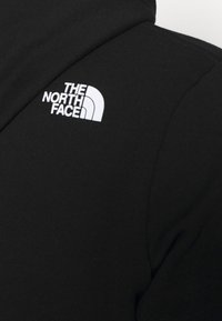 Giacca in pile nero con cappuccio arrotondato, texture liscia e logo bianco prominente di "The North Face" sulla spalla.