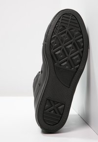 Schwarze Gummisneaker-Sohle mit einem geometrischen Profil, einer glatten Kante und einer strukturierten Oberfläche. Branding auf der Unterseite sichtbar.