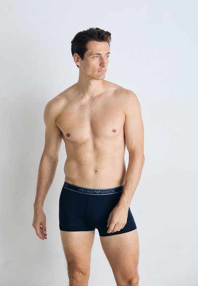 Svart boxershorts med elastisk midje som har "EMPORIO ARMANI" i grå tekst. Stoffet ser glatt og tettsittende ut.