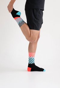 Bunte Socken mit schwarzen, türkisfarbenen und korallenfarbenen Streifen; schwarzer Sockenkörper mit türkisfarbenem Zeh und korallenfarbener Ferse. Reflektierendes Design.