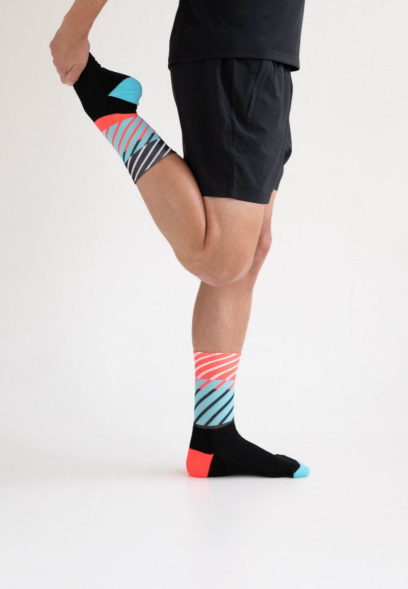 Bunte Socken mit schwarzen, türkisfarbenen und korallenfarbenen Streifen; schwarzer Sockenkörper mit türkisfarbenem Zeh und korallenfarbener Ferse. Reflektierendes Design.