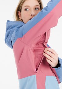 Giacca color block in rosa e blu con una ventilazione con zip. Presenta una fodera in rete traspirante, un cappuccio regolabile e una texture del tessuto liscia.