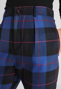 Pantalons taille haute à carreaux bleu et noir avec des plis ; présentent des lignes d'accent rose et une ceinture standard avec une poche latérale.