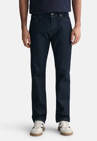 Jeans in denim blu scuro con taglio dritto, design a cinque tasche e cuciture a contrasto. Indossati con sneaker chiare.