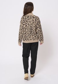 Brun leopardmönstrad tröja med ribbad krage, ihopparad med svarta tapered byxor och beige klackiga stövlar. Enkla vita bakgrund.