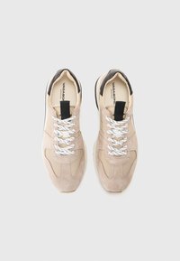 Beige suede sneakers with mesh accents, featuring white laces, a black accent at the heel, and a pull tab on the tongue.