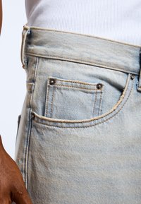 Jasnoniebieskie dżinsy o teksturowanym wykończeniu, z podwójnym przeszyciem, wyraźnym paskiem w talii oraz detalem tylnej kieszeni.