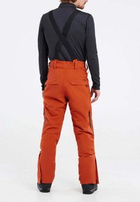 Oranga skidbyxor med justerbara remmar, dragkedjefickor och förstärkta nederkanter. Tillverkade av slitstarkt material, med en mjuk yta och en åtsittande design.