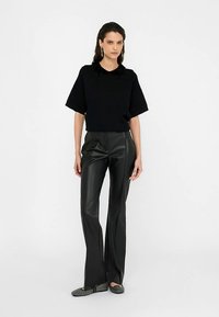 Zwarte top met korte mouwen en een versierde kraag, gecombineerd met hooggetailleerde zwarte flared broek van nep leer en grijze textuur schoenen.