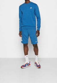 Sweatshirt et shorts Nike bleus en tissu assorti, accents de logo blancs. Baskets Nike rouges et bleues avec des détails blancs et semelles noires.