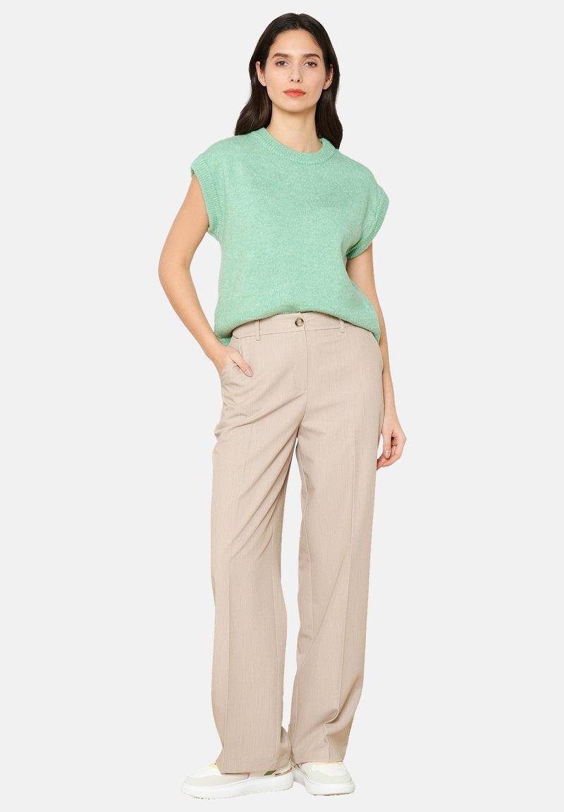 Minta zelena kratka majica iz trikotaže, bež visoko strukirane hlače s prednjim džepovima i bijele tenisice s suptilnim naglascima.