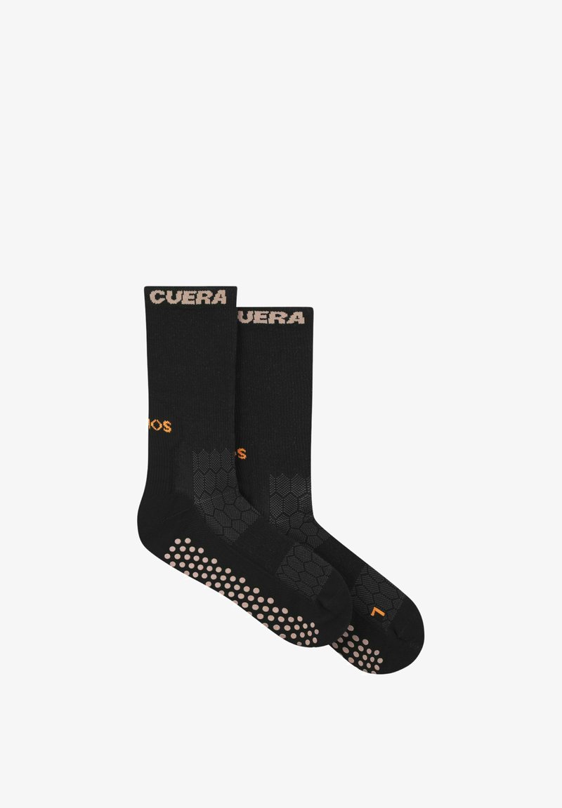 Paire de chaussettes noires mi-mollet avec des points antidérapants beiges sur les semelles, motif hexagonal sur le pied et texte beige sur le bord supérieur.