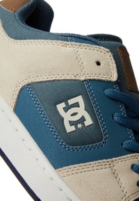 Baskets bleu et beige en suède et textile, avec une semelle blanche, des lacets bleus et un grand patch logo gris.