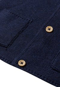 Navy gestrickte Strickjacke mit zwei Vordertaschen, einem strukturierten Gewebe und hellen Knöpfen mit einem dunklen Sternmotiv.