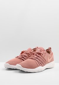 Różowe siateczkowe buty treningowe z teksturowaną cholewką, białą podeszwą i tonalnym logo Nike. Posiadają bezpieczny system sznurowania oraz wyściełany kołnierz.