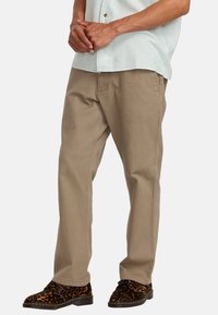 Chinos en coton beige avec une coupe droite. Ils comprennent deux poches latérales, une texture subtile et sont assortis à des chaussures à imprimé léopard.