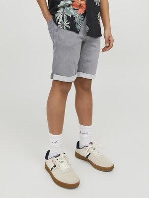Grijze denim shorts met opgerolde zoom, gecombineerd met witte sneakers en geribbelde witte sokken. De top heeft een zwart bloemenpatroon met levendige kleuren.