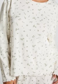 Witte lange mouwen top met een ribbelstructuur, voorzien van een groene bloemenprint. Golvende zoom aan de mouwen, casual pasvorm.