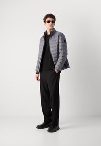 Gray puffer jacket with horizontal stitching, high collar, and black accents. Worn over a black shirt with relaxed-fit black trousers and black shoes.