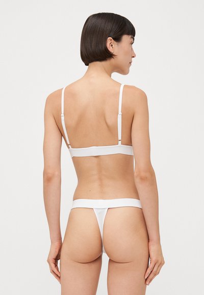 Set di lingerie bianco composto da un reggiseno semplice con spalline regolabili e un perizoma abbinato. Texture liscia e design minimalista senza decorazioni.