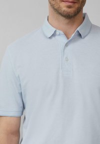 Hellblaues Polohemd aus strukturiertem Stoff mit Kragen, Drei-Knopf-Leiste und kurzen Ärmeln.