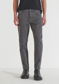 Jeans de mezclilla gris con corte recto, diseño de cinco bolsillos y un ligero desvanecimiento. Combinados con botas negras hasta el tobillo, mostrando una apariencia pulcra.