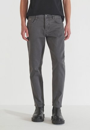 Jeans de mezclilla gris con corte recto, diseño de cinco bolsillos y un ligero desvanecimiento. Combinados con botas negras hasta el tobillo, mostrando una apariencia pulcra.