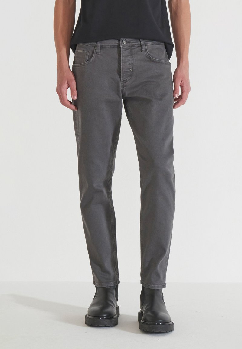 Jeans de mezclilla gris con corte recto, diseño de cinco bolsillos y un ligero desvanecimiento. Combinados con botas negras hasta el tobillo, mostrando una apariencia pulcra.