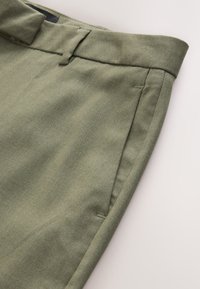 Oļīvzaļas bikses ar teksturētu audumu, taisnu griezumu, sānu kabatām un jostu ar slēptu aizdari.
