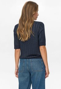 Kortärmad marinblå ribbad topp med metalltrådar, ihopparad med högmidjade blå jeans, som visar bakvyn och avslappnad passform.