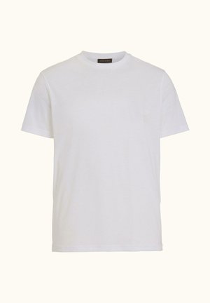 T-shirt blanc uni à manches courtes et col rond, avec une petite étiquette noire au niveau du col, présenté sur un fond beige clair.