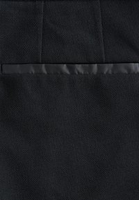 Tissu noir texturé avec une bande horizontale lisse en satin noir cousue au milieu, montrant un contraste détaillé des matériaux.