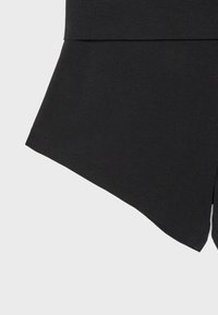 Gros plan sur un tissu noir montrant la couture et l'ourlet d'un vêtement avec un léger évasement au bas.