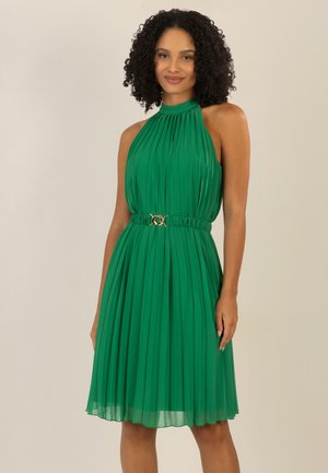 Grünes Faltenkleid mit hohem Ausschnitt und tailliertem Bund, das einen goldenen Akzent aufweist. Leichter Stoff, knielang, glatte Textur.