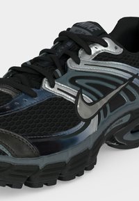 Μαύρο και γκρι αθλητικό παπούτσι Nike με επάνω μέρος από διχτυωτό υλικό, μαλακή σόλα και κορδόνια, φαίνεται το πλάι με ορατό το λογότυπο swoosh.
