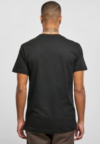 Sort bomulds T-shirt med korte ærmer, rund hals og en glat tekstur. Viser detaljer af ryggen og en tatovering på halsen.