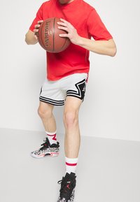 Person in red shirt and white basketball shorts holding a Spalding basketball in a ready stance on plain background.